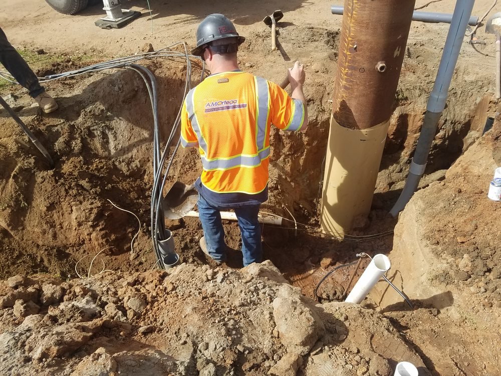 Electrician routing underground conduit at the base of a service pole